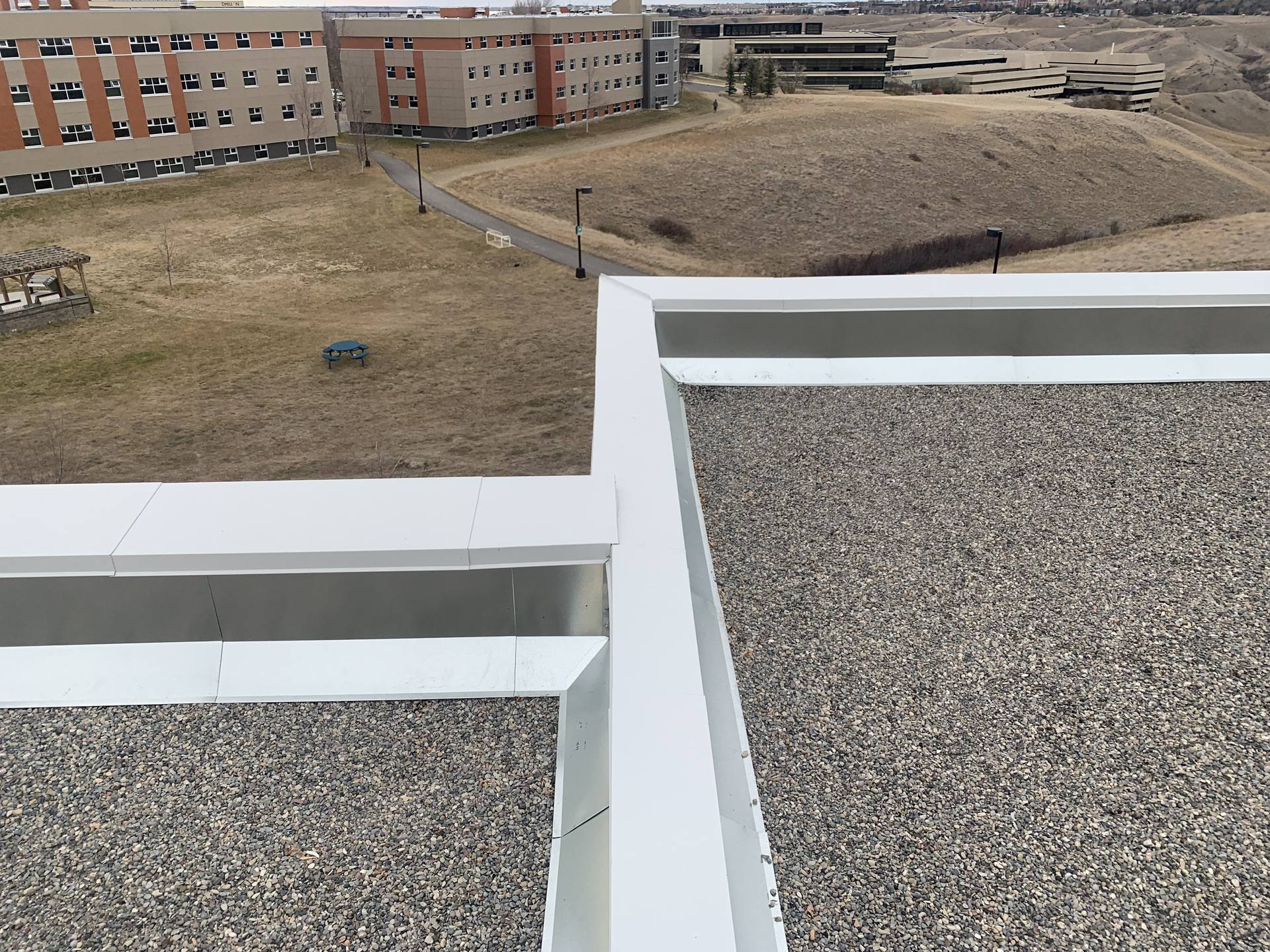 Gravel ballast and white cap flashing on a C & H low-slope roof, the coulees beyond