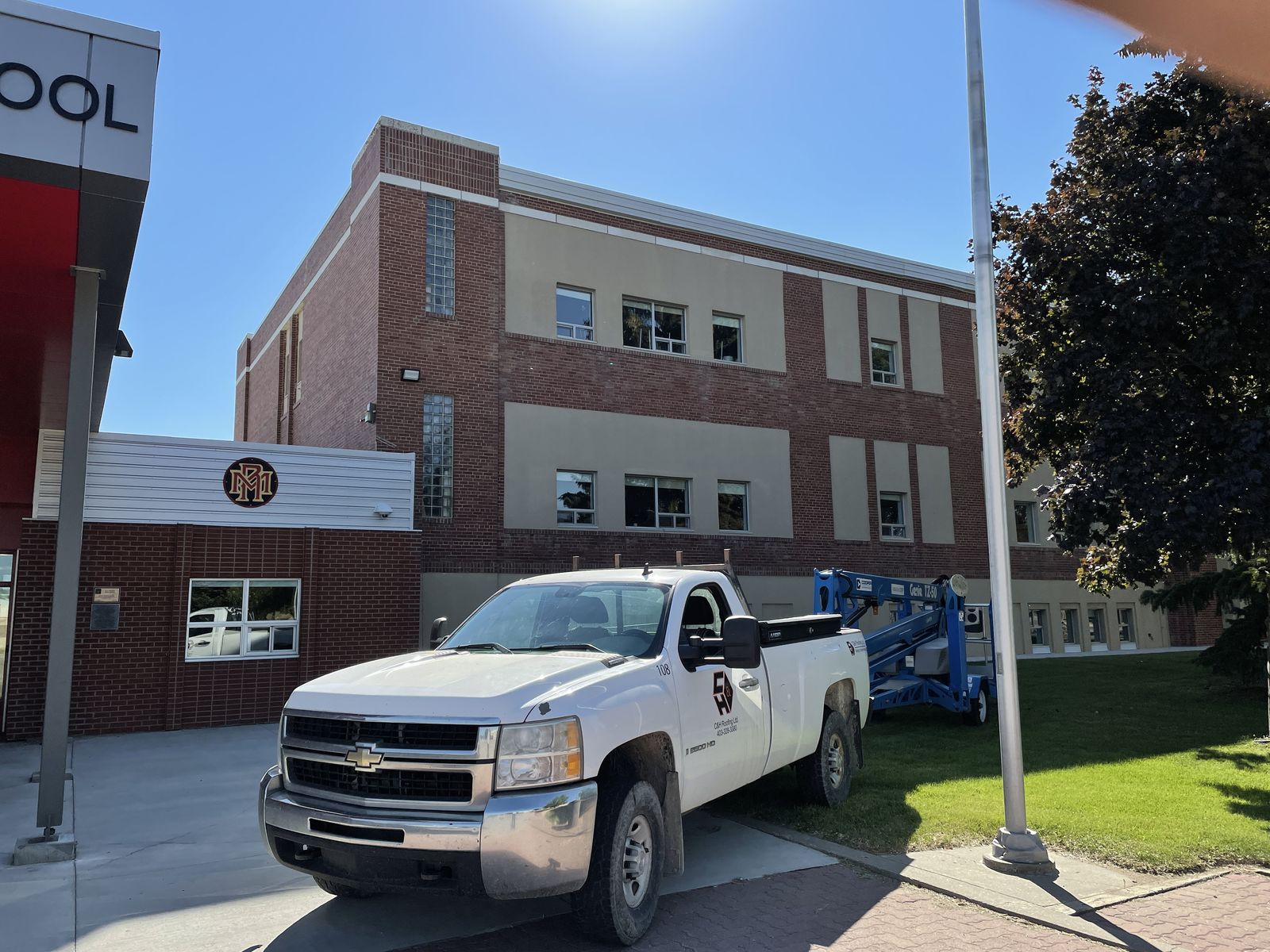 A C & H Roofing truck parked at a Lethbridge school beside a boom lift